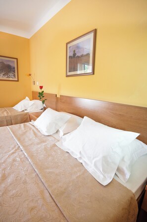 A hotel room with two beds, a wooden headboard, a framed picture on the wall, and a vase with a rose.