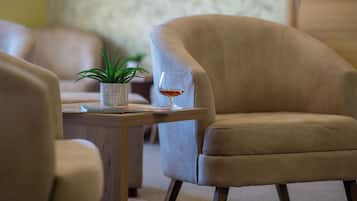 Una habitación con un sillón beige, una mesita con un vaso de líquido ámbar y una planta en maceta.