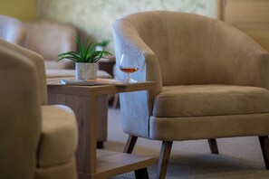 A room with a beige armchair, a small table with a glass of amber liquid, and a potted plant.