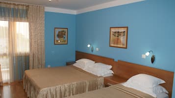Hotellihuone, jossa on kaksi sänkyä, puinen pääty, yöpöytä, lamppu ja kaksi kehystettyä kuvaa seinällä.