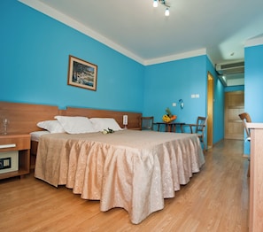 Een hotelkamer met een bed, een nachtkastje, een bureau, een stoel en een kleine tafel met fruit.
