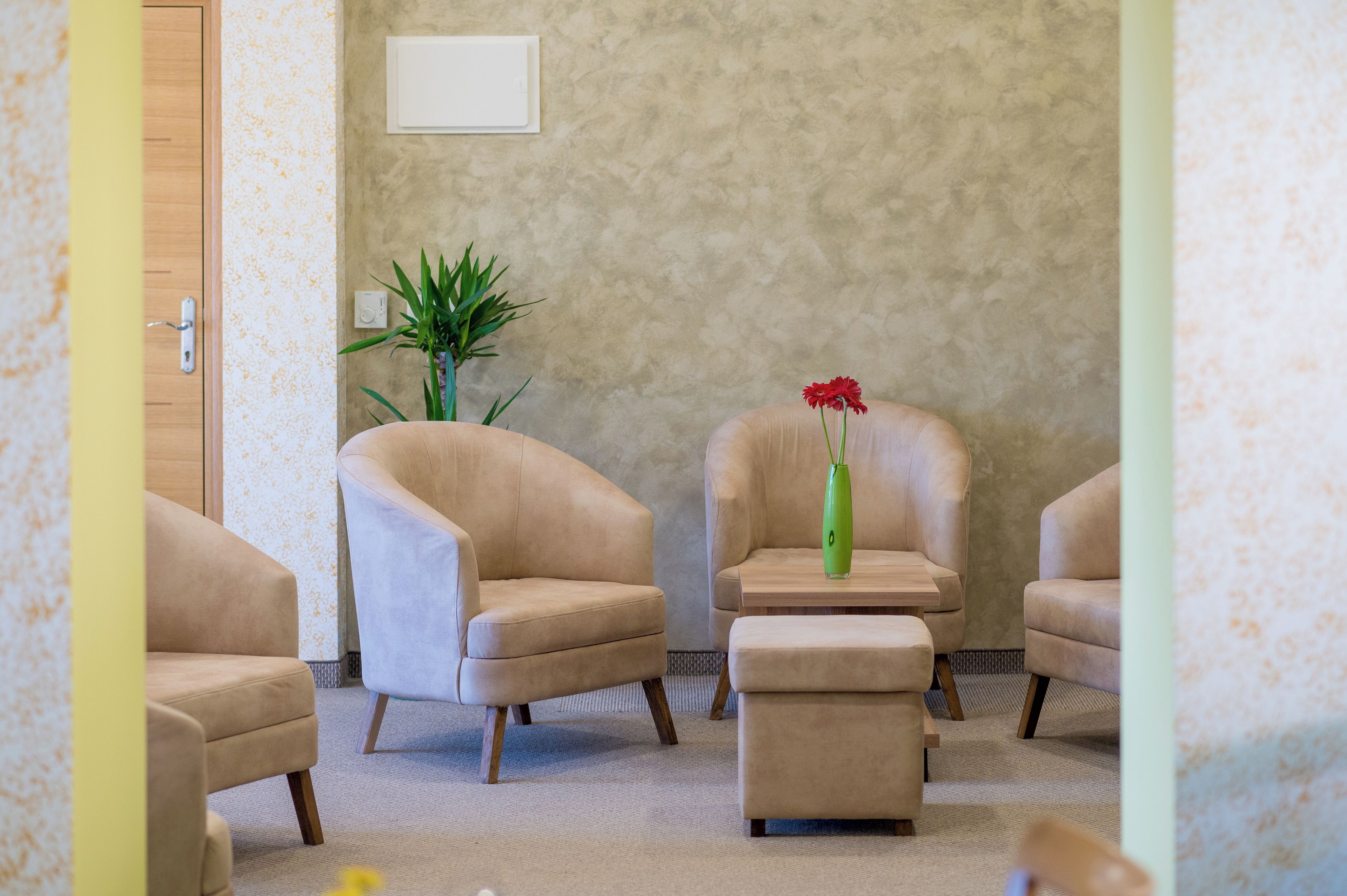 Une pièce avec des fauteuils beiges, une petite table et un vase vert contenant des fleurs.