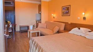 Ein Hotelzimmer mit einem großen Bett, einer Couch, einem kleinen Tisch, einem Stuhl und einer Küchenzeile.