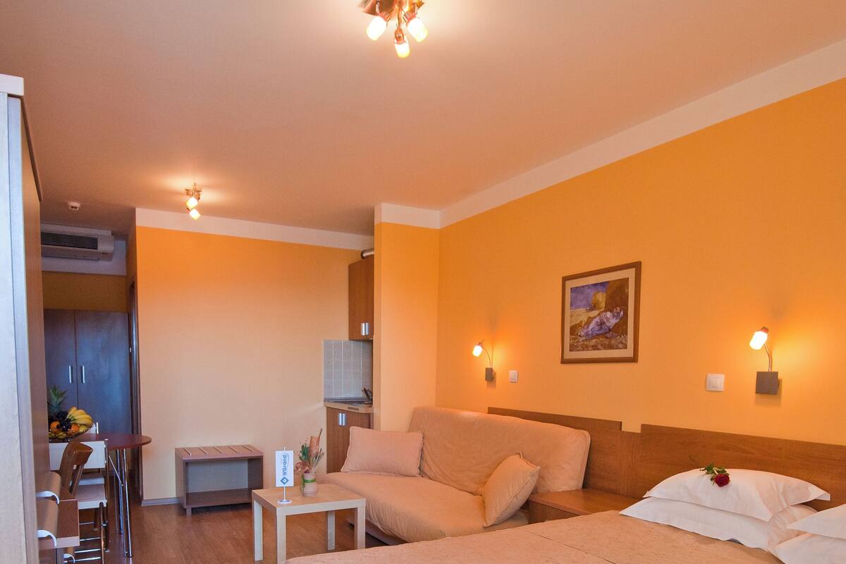 Una habitación de hotel con una cama grande, un sofá, una mesita, una silla y una zona de kitchenette.