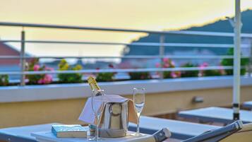 A table with a bottle of champagne, a glass, and a book on a terrace with a view of the sunset.