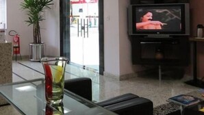 Een hotel lobby met een glazen tafel, een kamerplant, een televisie op een standaard en een brandblusser.