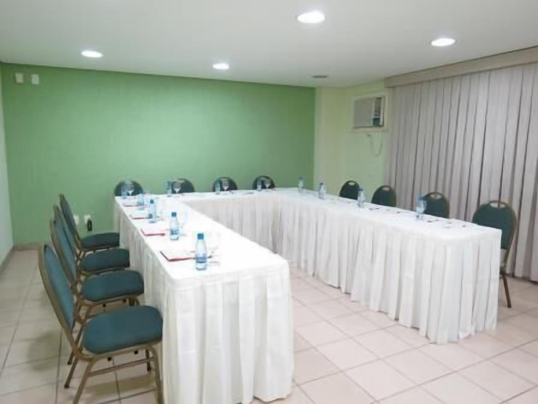 Uma sala de conferências com uma mesa comprida, cadeiras e garrafas de água.