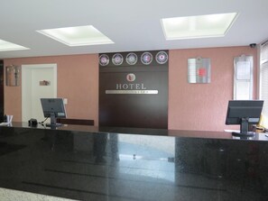 A hotel reception desk with a modern design, including a black counter and a digital display. - Steel Valley Hotel (Ipatinga)