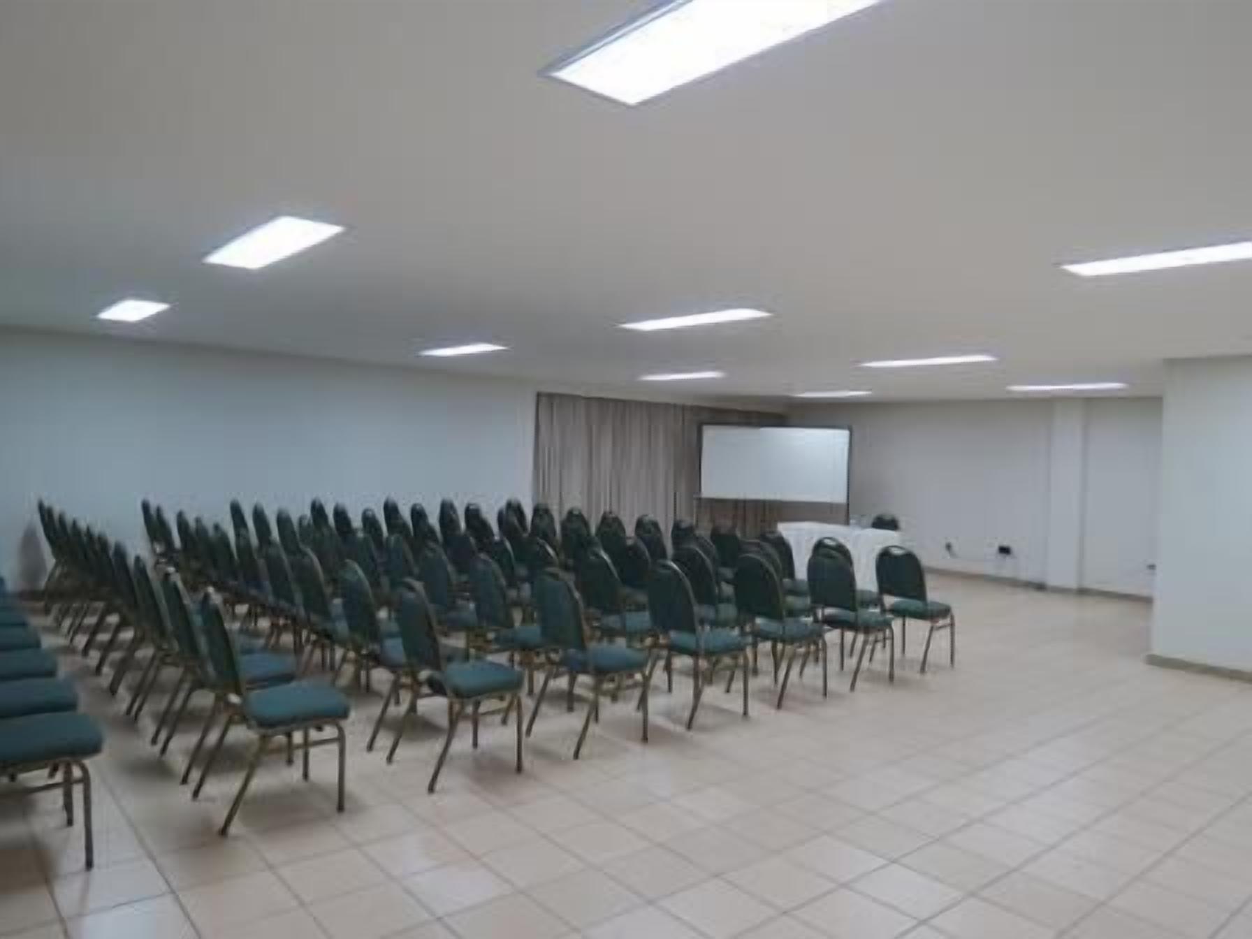 A conference room with rows of chairs, a projector screen, and a whiteboard.