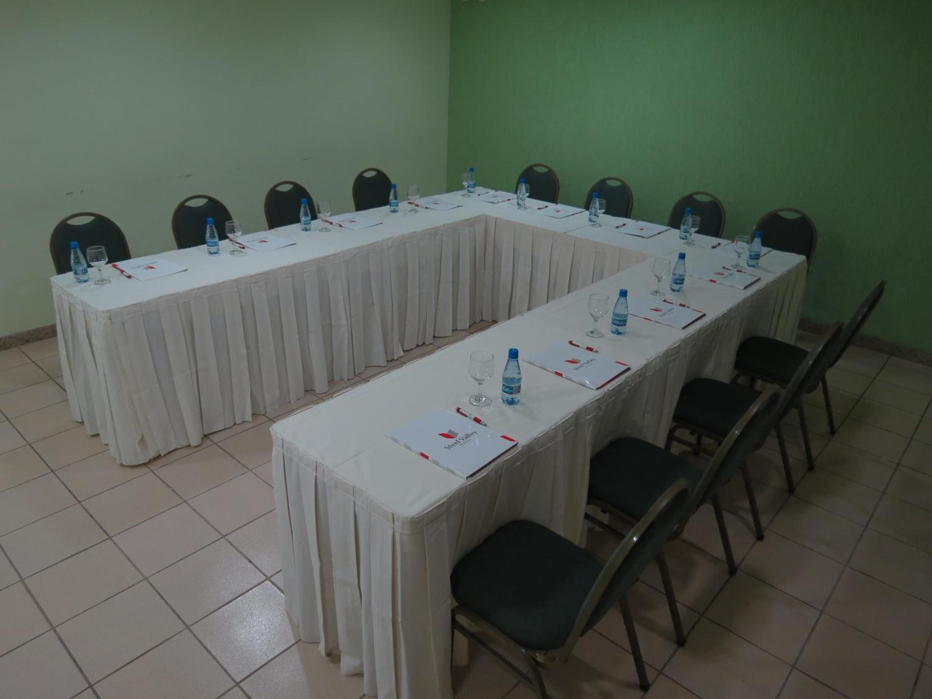 Uma sala de conferência com uma mesa comprida, cadeiras, garrafas de água e documentos.