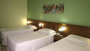Een hotelkamer met drie eenpersoonsbedden, elk met een houten hoofdbord en nachtlampjes.