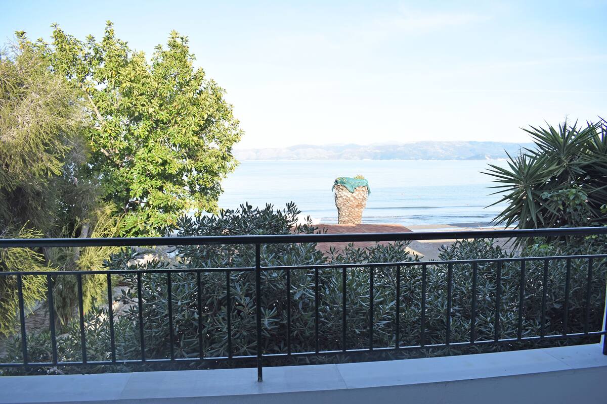 A balcony with a view of the sea, surrounded by greenery and a metal railing.