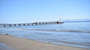 A beach with a long pier extending into calm waters, a clear sky, and distant mountains. - Akti Panela Beach Hotel (Corfu)