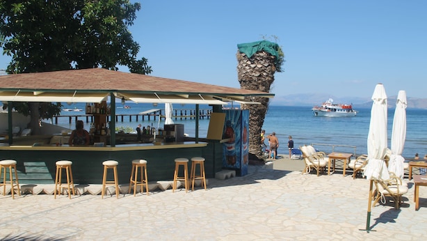 An outdoor bar area with stone flooring, wooden stools, and umbrellas. - Akti Panela Beach Hotel (Corfu)