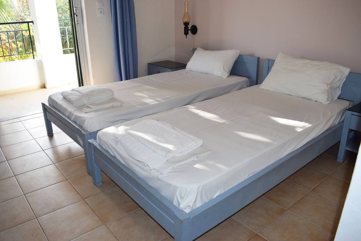 A double bed with white linens and a blue headboard in a room with tiled flooring.