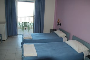 Habitación de hotel con dos camas, un balcón con sillas y vistas al exterior.