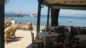 An outdoor dining area with tables and chairs, overlooking a body of water with boats. - Akti Panela Beach Hotel (Corfu)