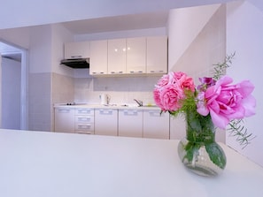 Una cocina moderna con armarios blancos, un lavamanos de acero inoxidable y un florero con flores rosadas sobre la encimera.