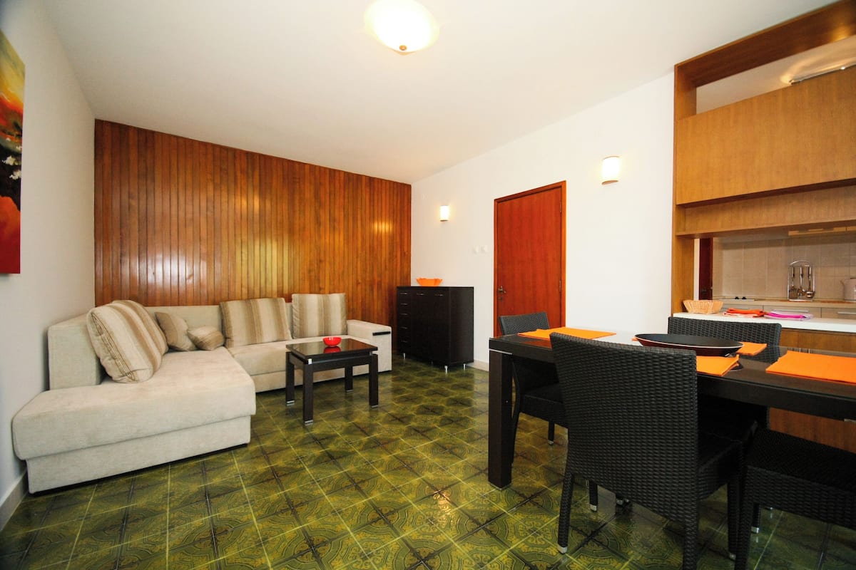 Una sala de estar con un sofá, una mesa de comedor con sillas, una zona de cocina y un suelo estampado.