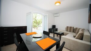 A modern living room with a glass door leading to a balcony, a sofa, a coffee table, and a dining table with orange placemats. - Villa Marijeta (Dubrovnik)