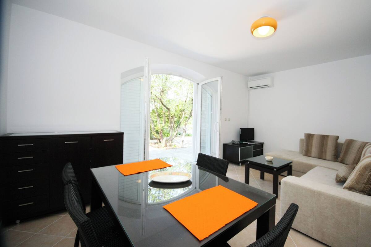 Una sala de estar moderna con un ventanal que da a un balcón, un sofá, una mesa de centro y una mesa de comedor con manteles individuales naranjas.