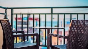 A balcony with wicker chairs and a small round table, overlooking a cityscape.