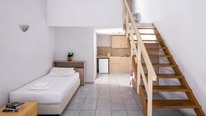 Een slaapkamer met een bed, nachtkastje en een klein plantje op het nachtkastje. Er is een houten trap die leidt naar een keuken met kasten en een koelkast.