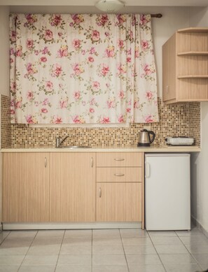A kitchen with wooden cabinets, a tiled backsplash, a small refrigerator, a kettle, and a toaster.