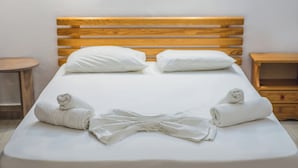 A neatly made bed with white linens and two pillows, a wooden headboard, and two bedside tables.