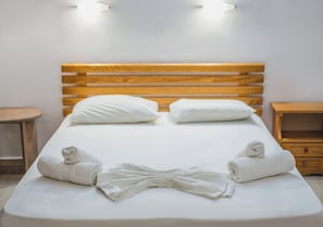 A neatly made bed with white linens and two pillows, a wooden headboard, and two bedside tables. - Stefania Studios (Hersonissos)