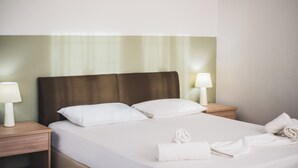 A neatly made bed with white linens, two bedside lamps, and a wooden nightstand.