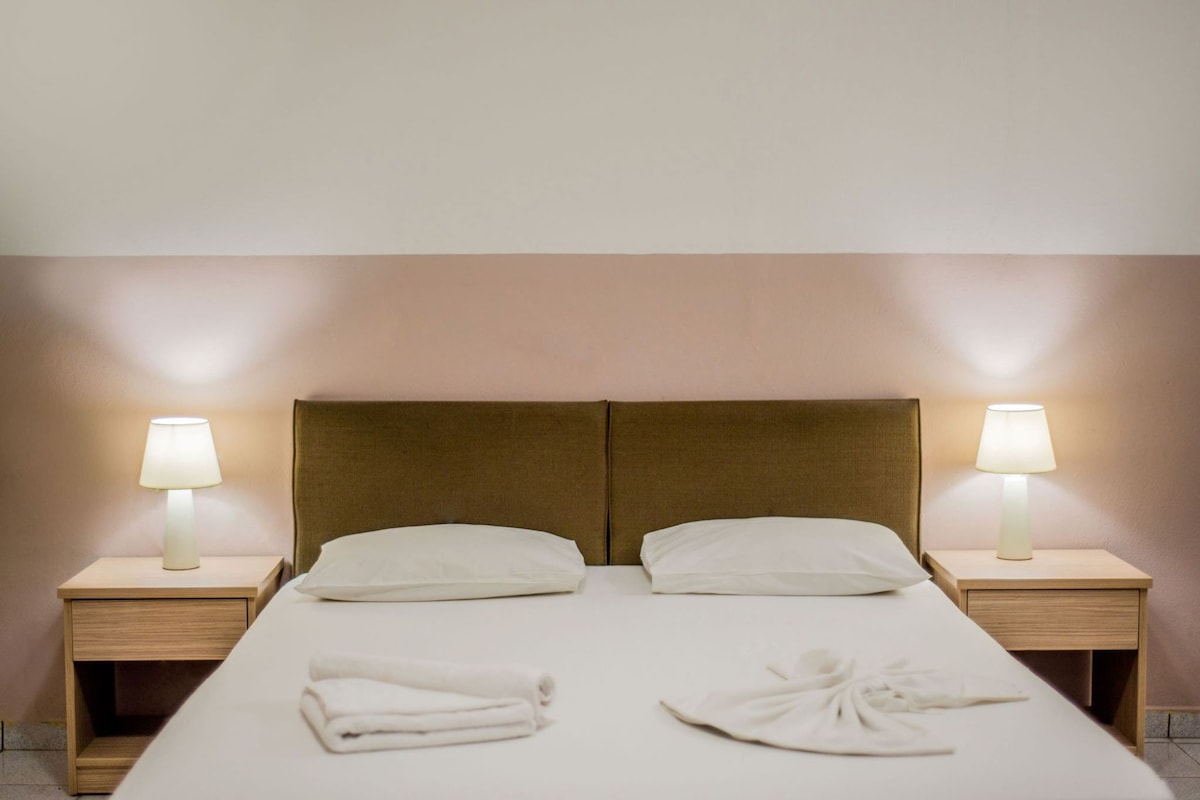 A neatly made bed with pillows, two bedside lamps, and folded towels on a clean, simple room.