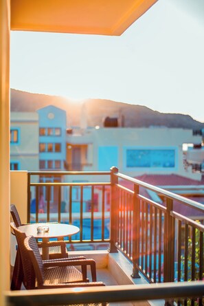 A balcony with a table and chairs, overlooking a building with a blue facade and a mountain in the background. - Stefania Studios (Hersonissos)