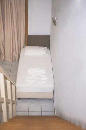 A small, single-bed room with a wooden staircase leading to a door. - Stefania Studios (Hersonissos)