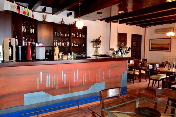 Zona de bar con estantes de madera llenos de botellas, una barra de diseño único y un comedor con mesas y sillas.