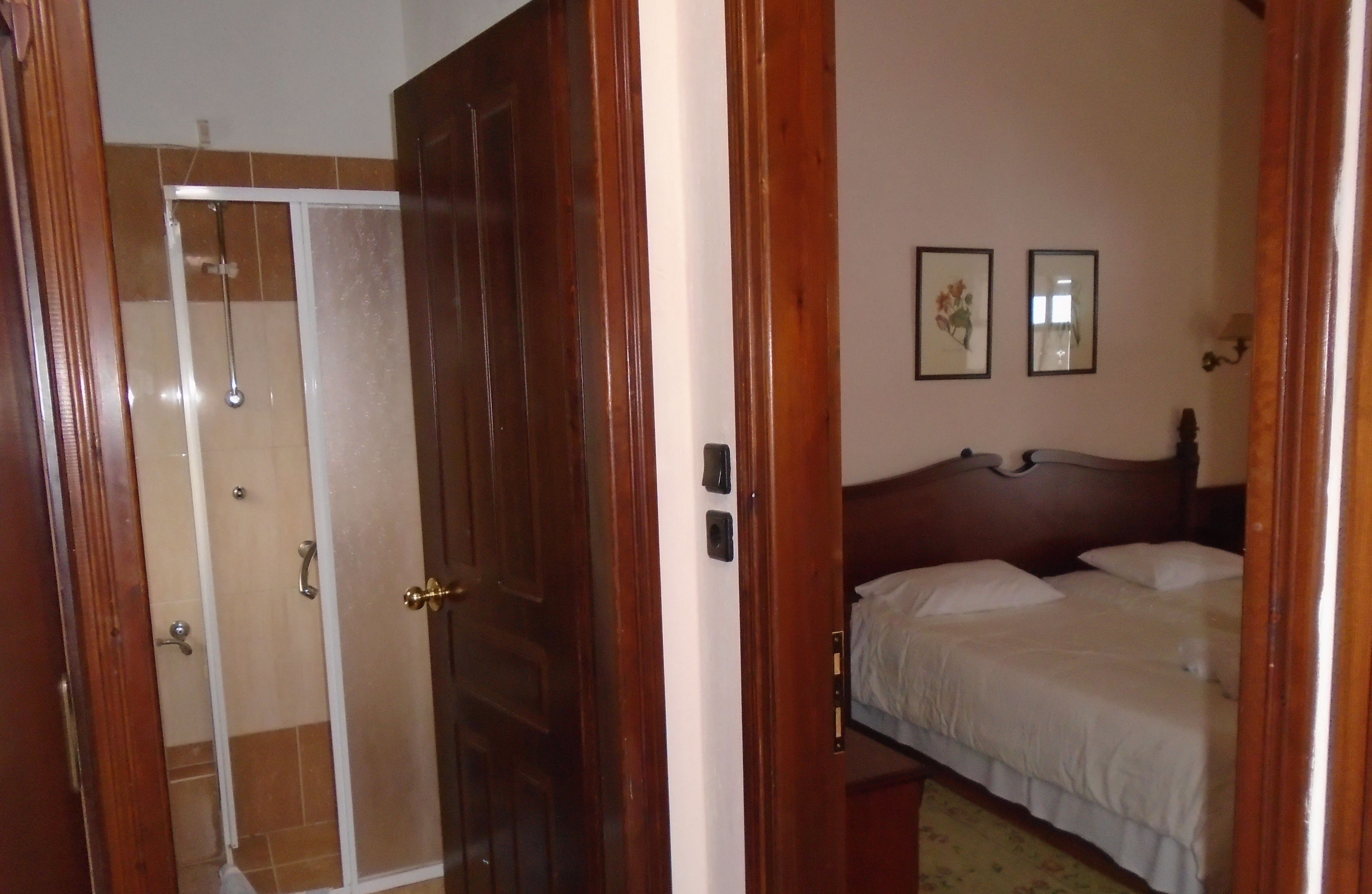 A bedroom with a wooden bed, a wooden wardrobe, and a shower area.