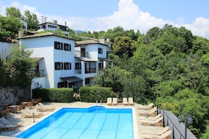A pool area with lounge chairs, a stone wall, and a building with multiple balconies. - Aglaida Hotel (Zagora-Mouresi)