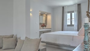 A bedroom with a bed, a sofa, a mirror, and a window. - Papadakis (Paros)