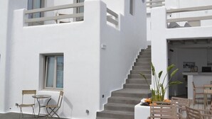 A modern white building with a staircase leading to a balcony, outdoor seating area, and a small table with chairs. - Papadakis (Paros)