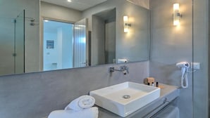 A modern bathroom with a large mirror, a white sink, a towel, and a hairdryer. - Papadakis (Paros)