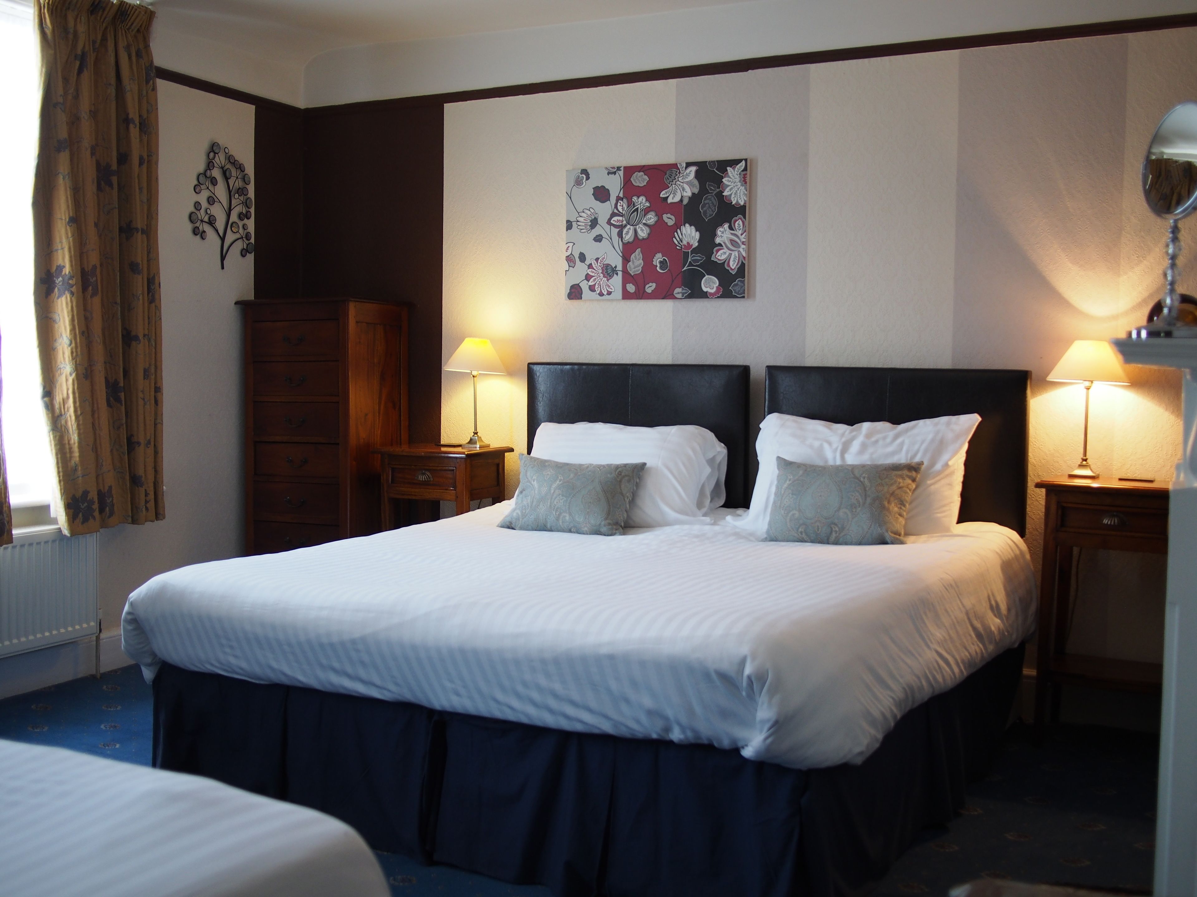 Una habitación de hotel con una cama grande, dos mesitas de noche con lámparas, un armario de madera y una obra de arte floral en la pared.