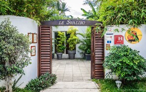 The entrance to Le Swalibo with a wooden archway, potted plants, and a wall with various signs and a logo. - Swalibo Hotel (Saint-Paul)