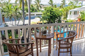 A wooden deck with two chairs and a table, overlooking a pool and lush greenery. - Swalibo Hotel (Saint-Paul)