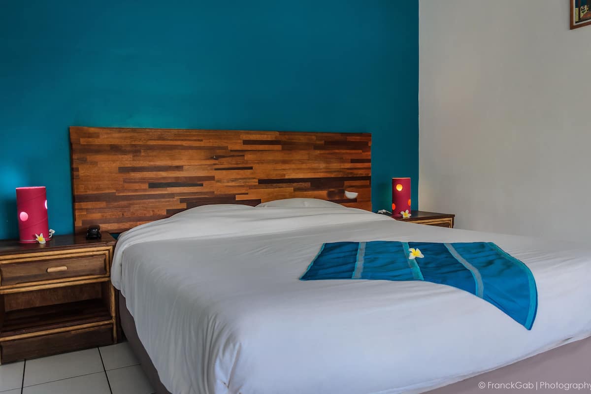 A neatly made bed with a blue accent pillow, wooden headboard, and two bedside tables with red lamps.