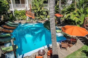 A pool area with lounge chairs, a wooden deck, and palm trees. - Swalibo Hotel (Saint-Paul)