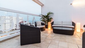 Un balcon agrémenté de meubles en osier, d’une plante en pot et offrant une vue sur le paysage urbain.