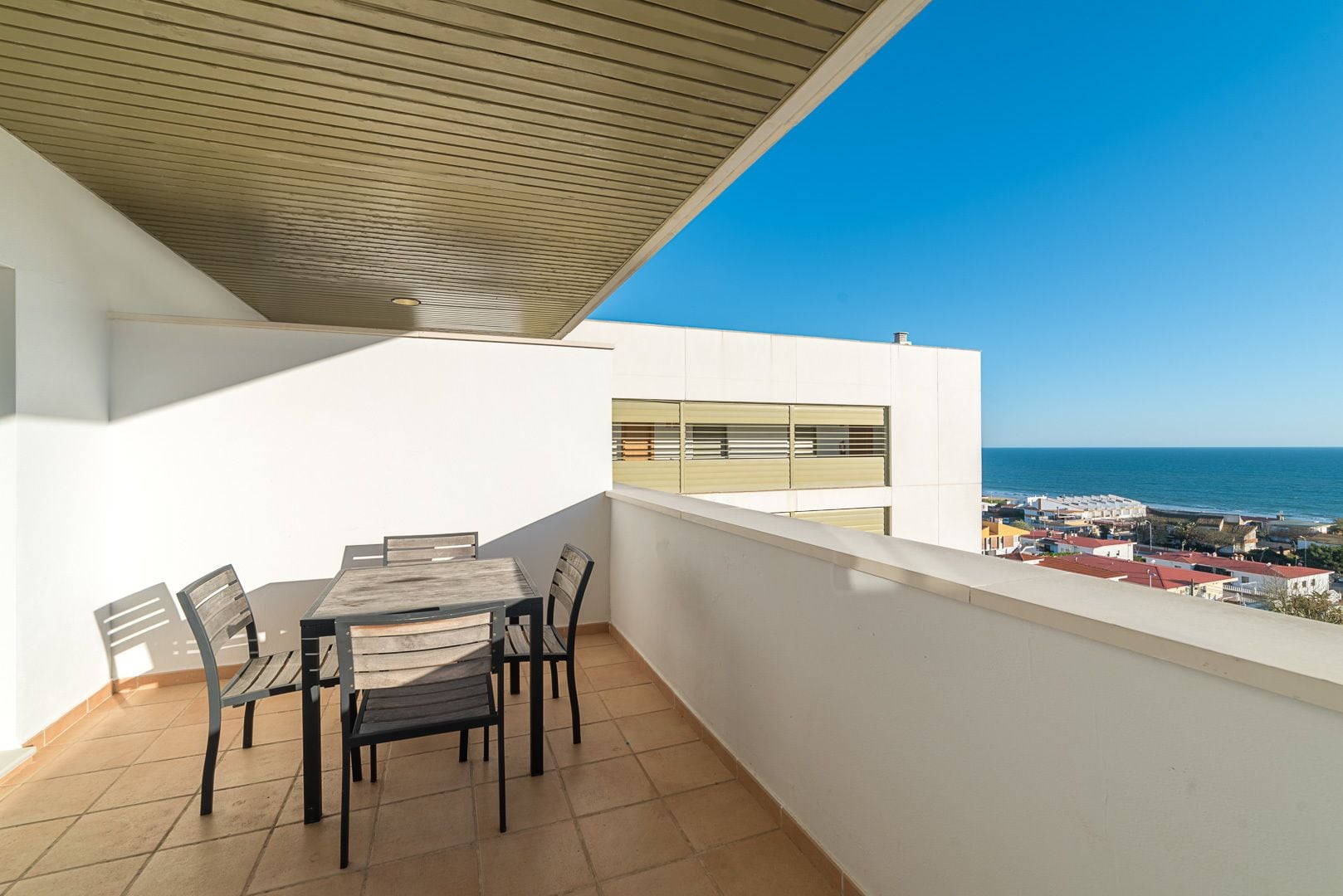 Un balcón con mesa y sillas, con vistas a un pueblo costero y al mar.