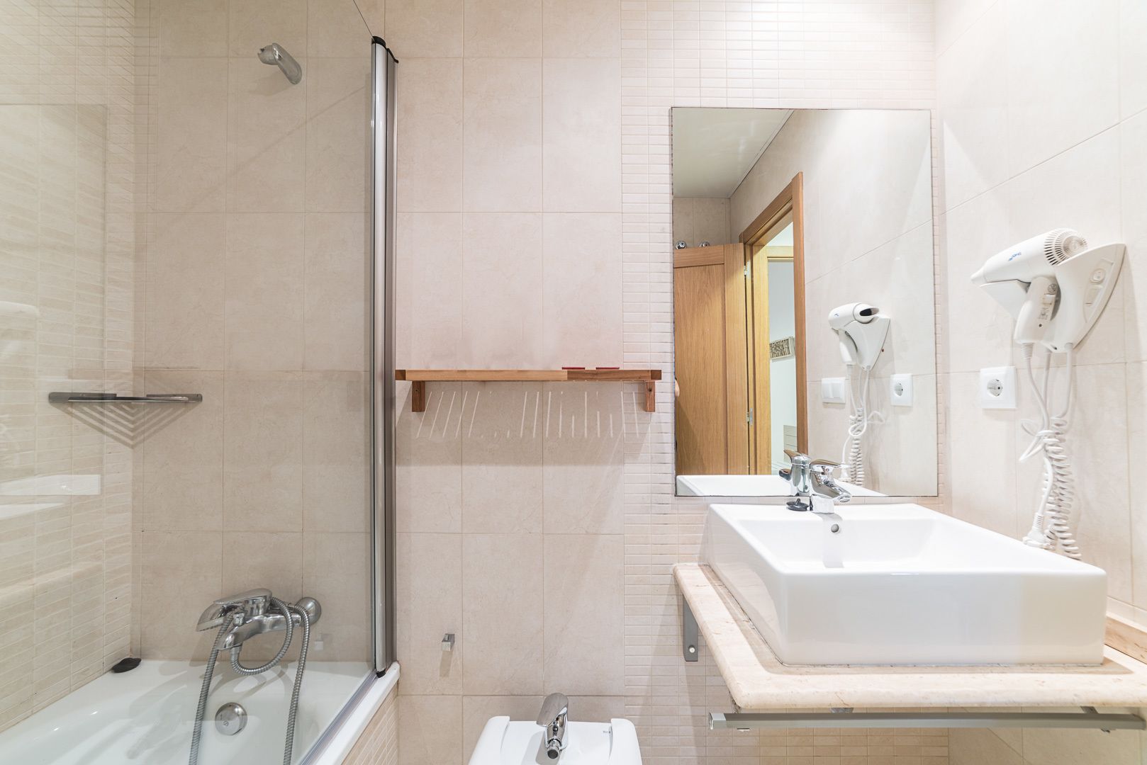 Un baño moderno con cabina de ducha de vidrio, un espejo grande, un lavamanos blanco y dos secadores de pelo fijos en la pared.