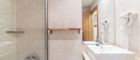 Un baño moderno con cabina de ducha de vidrio, un espejo grande, un lavamanos blanco y dos secadores de pelo fijos en la pared.
