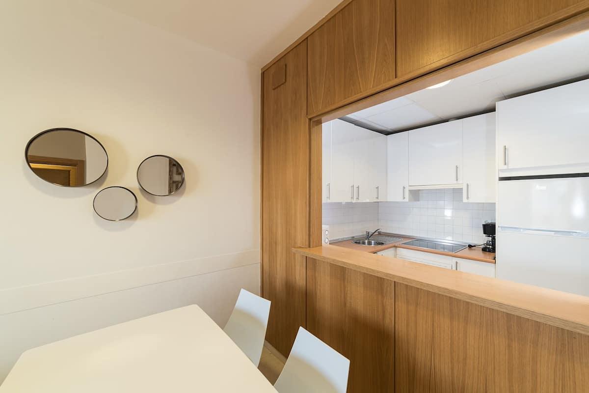 A modern kitchen with white cabinets, a wooden countertop, and a large mirror.